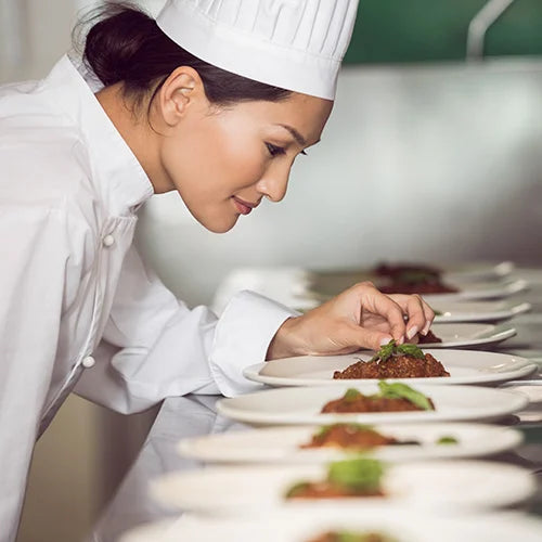 Chef garnishing plates of food in a professional kitchen setting